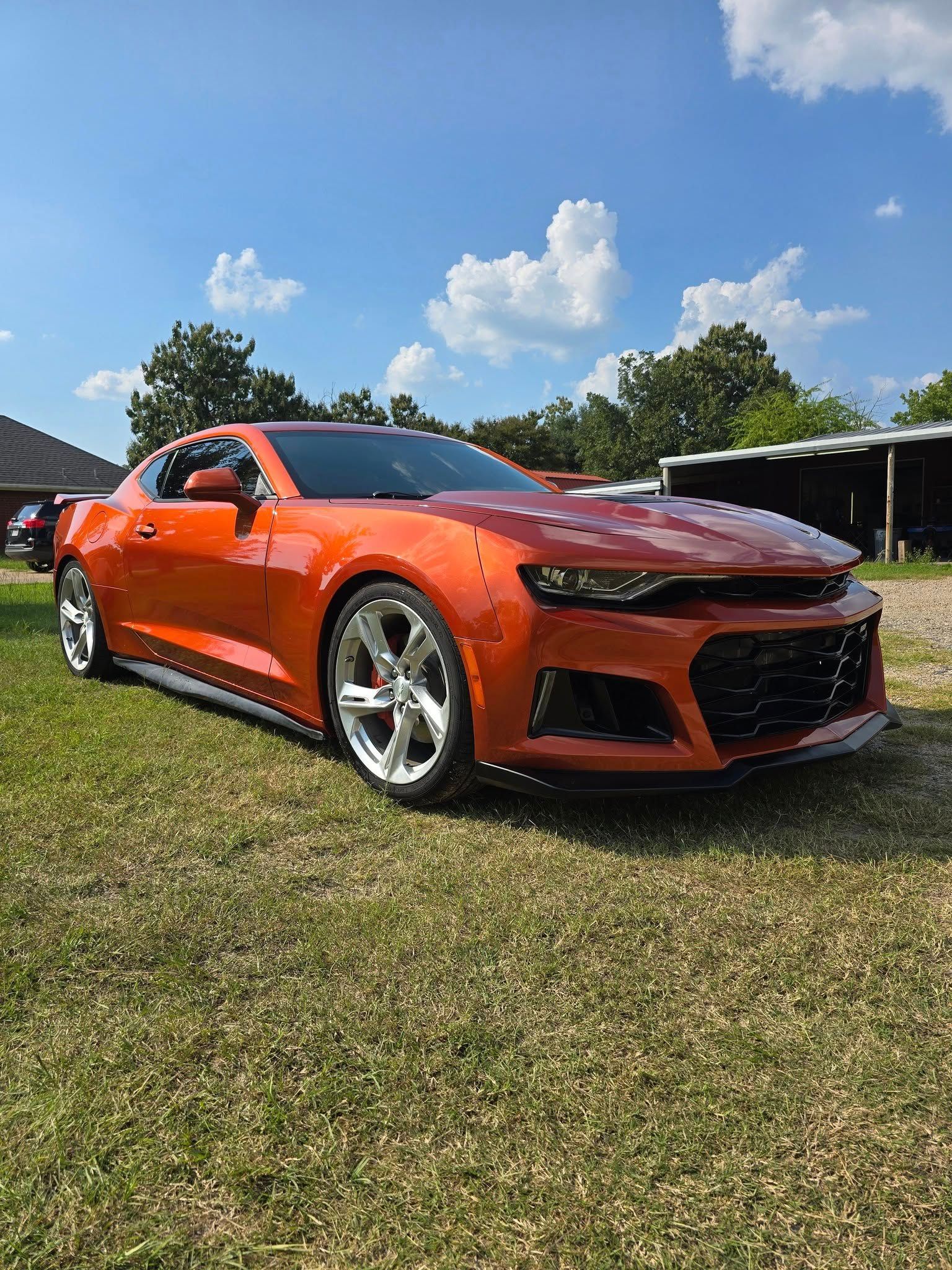 Orange sports car parked on grass under a blue sky.