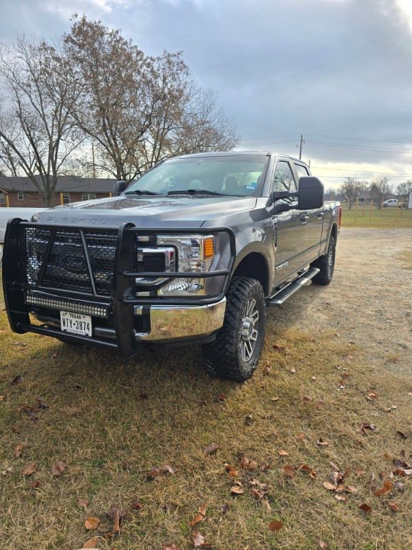 Black pickup truck with grille guard parked on grass near a house under a cloudy sky
