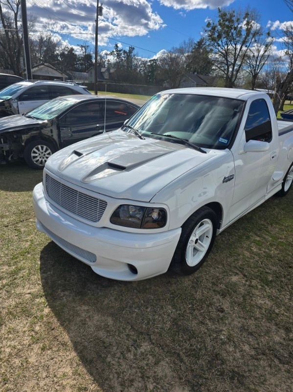 White pickup truck parked on grass beside other vehicles under a partly cloudy sky