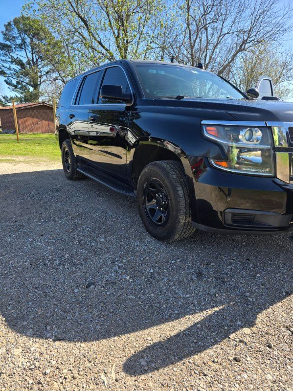 Black SUV parked on gravel driveway beside a brick wall, with trees and blue sky in the background