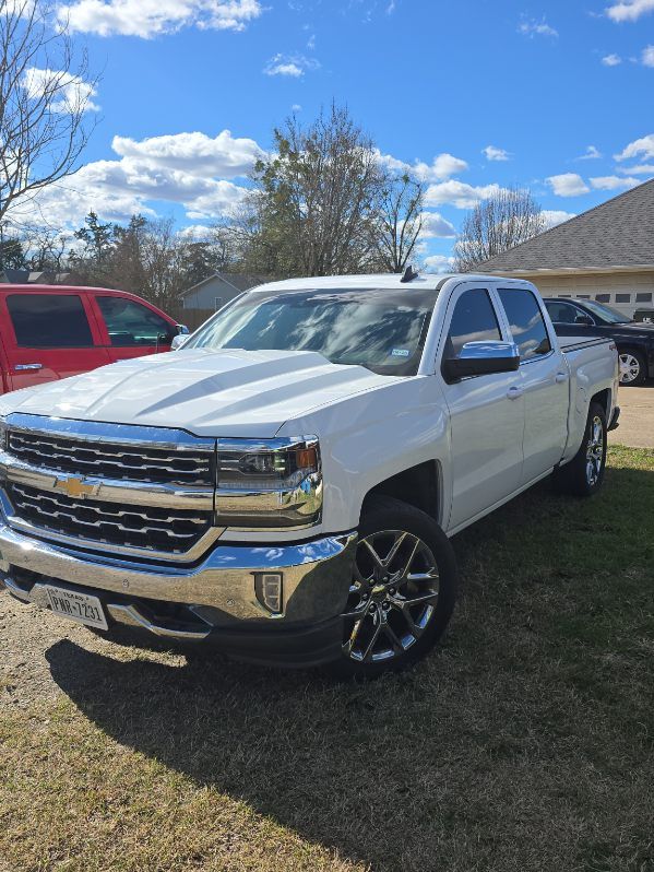 White Chevrolet Silverado truck parked on grass under a blue sky, with a red vehicle beside it.