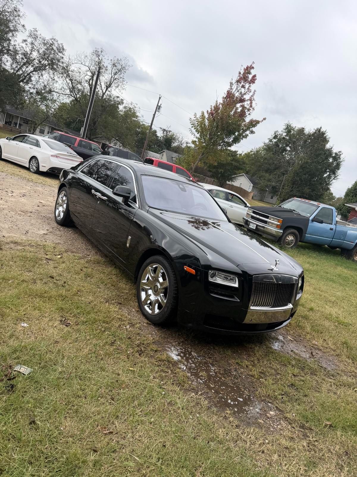 Black sedan parked on grass at an outdoor lot, with other cars and trees in the background.