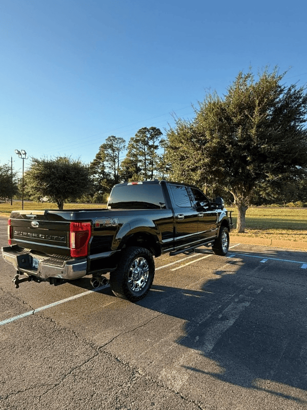 Black pickup truck parked on a sunny road near trees, with a trailer hitch attached.