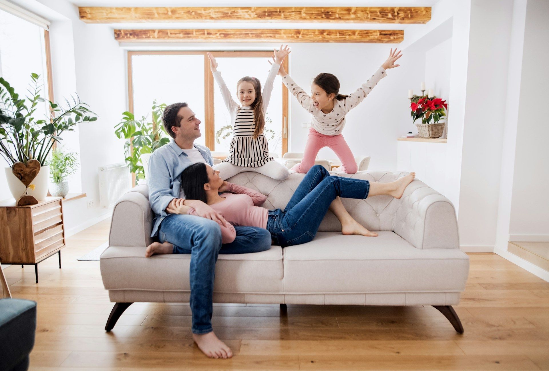 Family relaxing on a beige sofa in a bright living room, with two children playing on the backrest