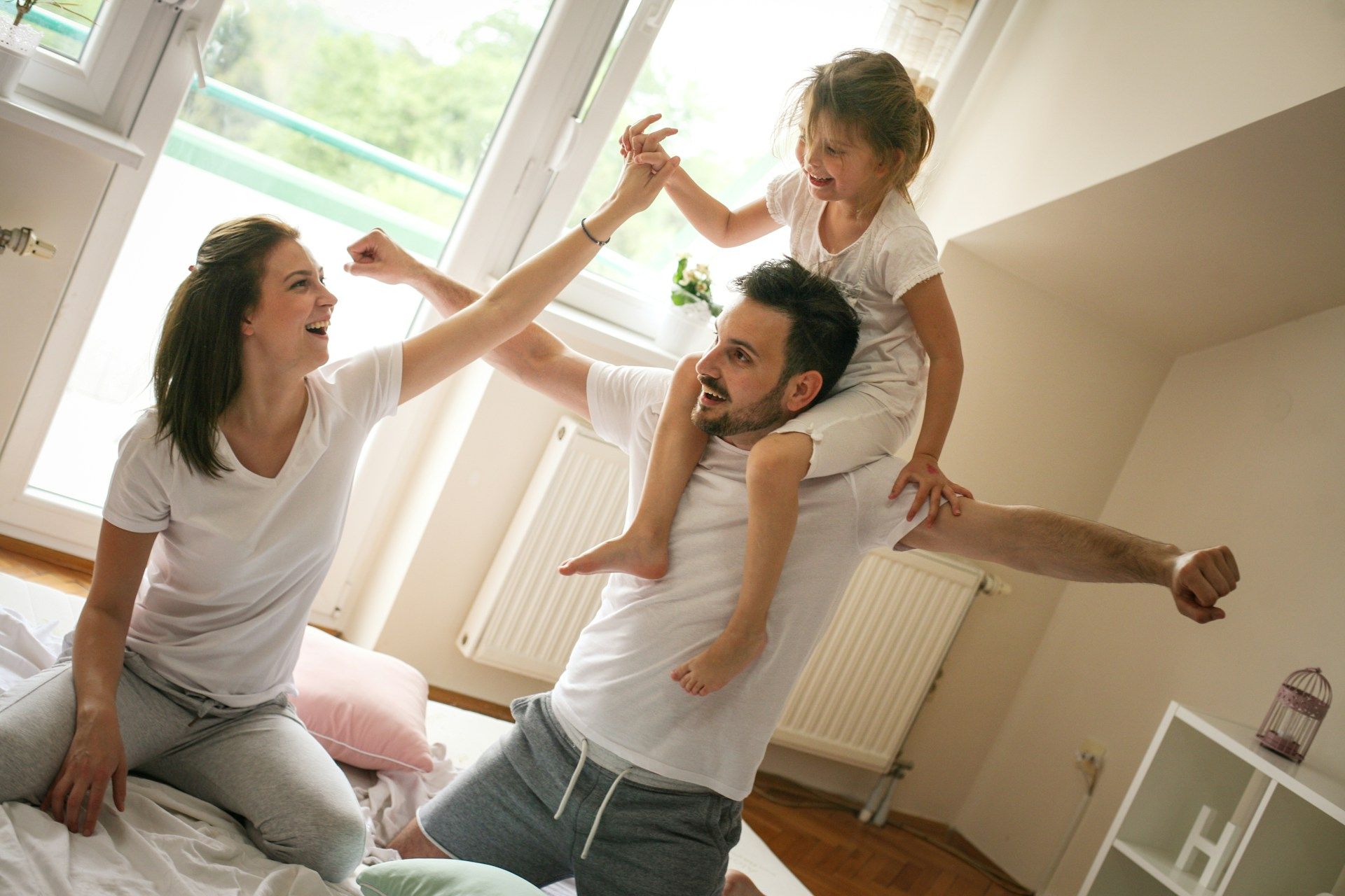 Smiling family playing together in a bright living room, with a child on an adult’s shoulders.