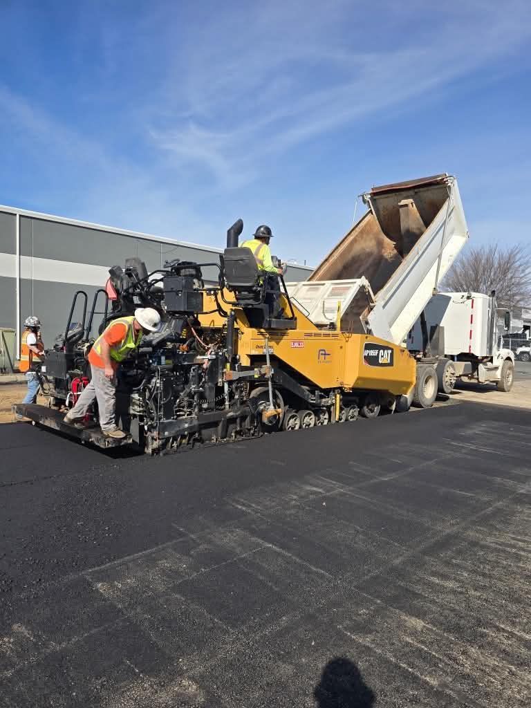 Road paving machine laying asphalt on a highway under blue sky, workers standing beside it