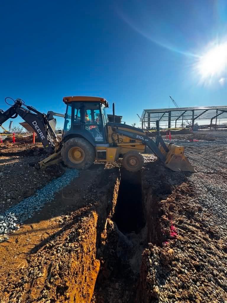 Backhoe excavator digging a trench in a gravel lot under a bright blue sky