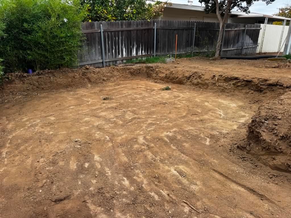 Cleared dirt lot with a wooden fence and trees along the edge