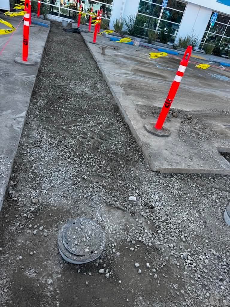 Construction walkway with gravel path, concrete edges, and red safety cones near a building entrance