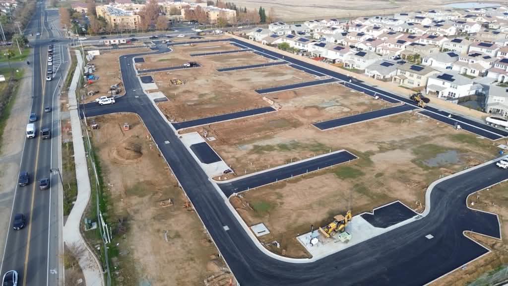 Aerial view of a new housing development with paved roads, empty lots, and surrounding homes.