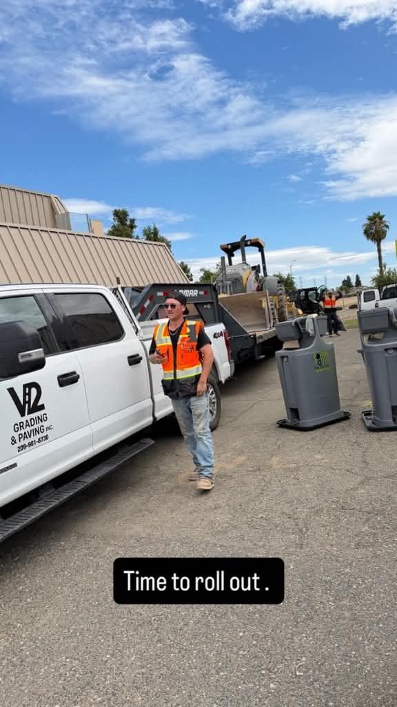 Workers loading a white van with trash bins in a parking lot under a blue sky