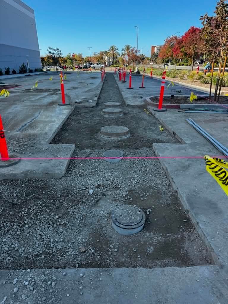 Construction zone with orange cones and a rough trench in a parking lot beside a building