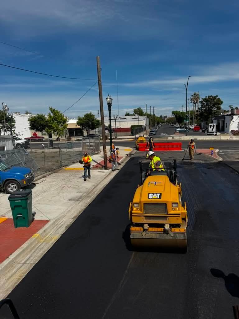 Roadwork with a yellow roller and workers paving a street under a clear blue sky
