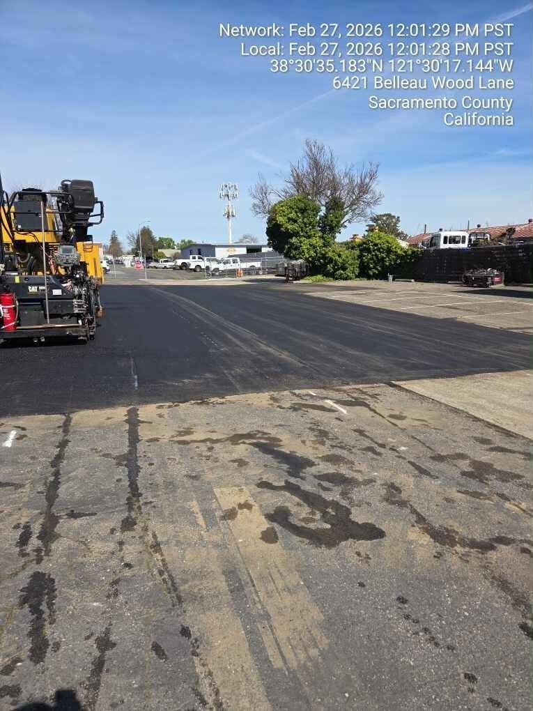 Roadwork vehicle on a sunlit street with lane markings and houses in the distance.