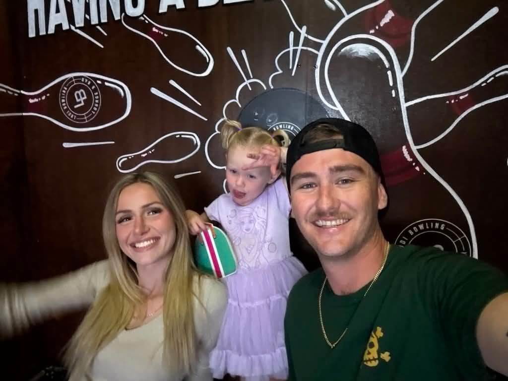 Three people posing in front of a chalkboard wall, smiling at a lively event.