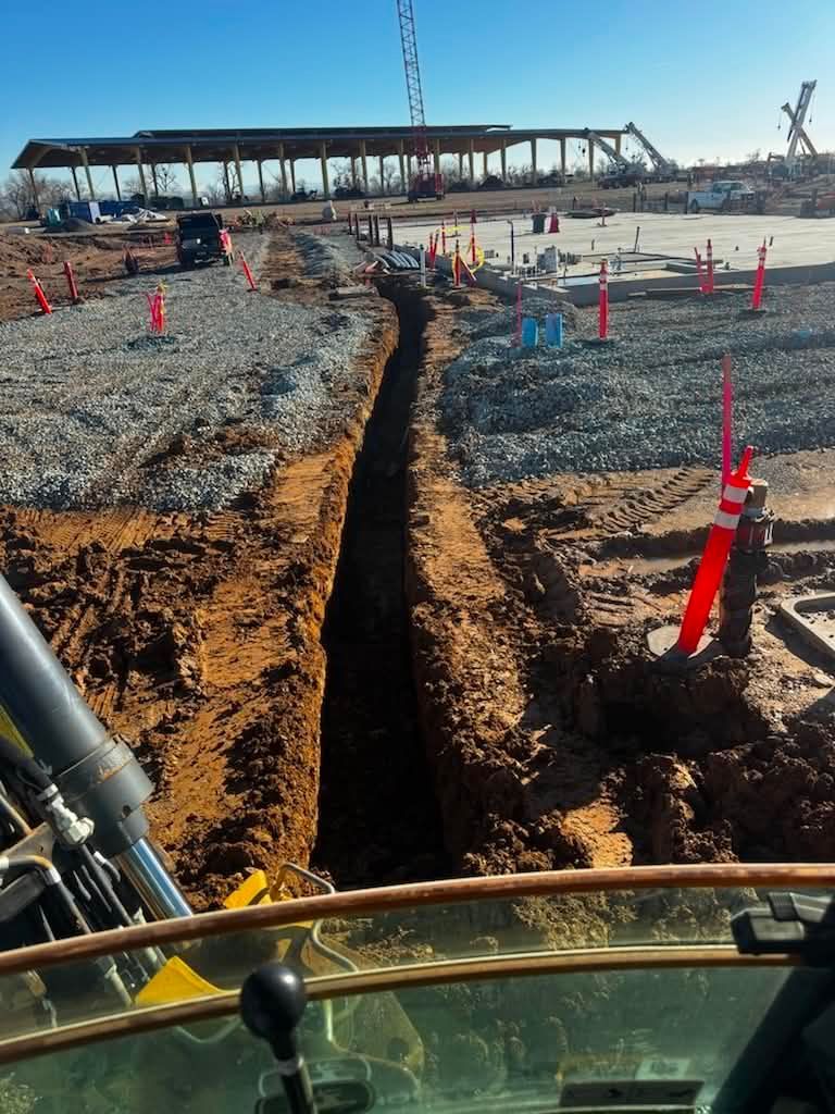 Trench excavation at a construction site with orange cones and a yellow machine in the foreground.