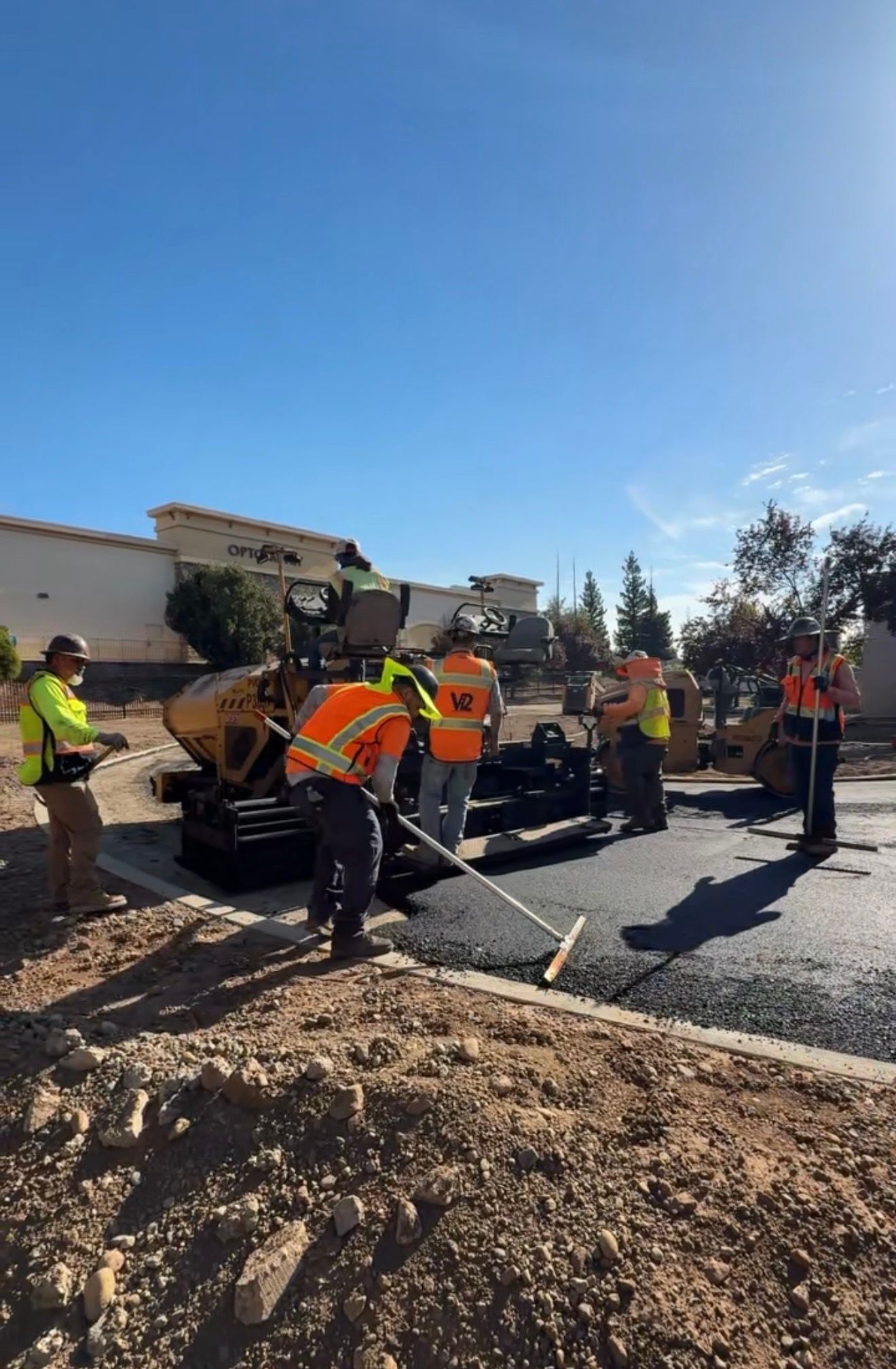 Road crew in orange vests paving asphalt on a sunny street construction site