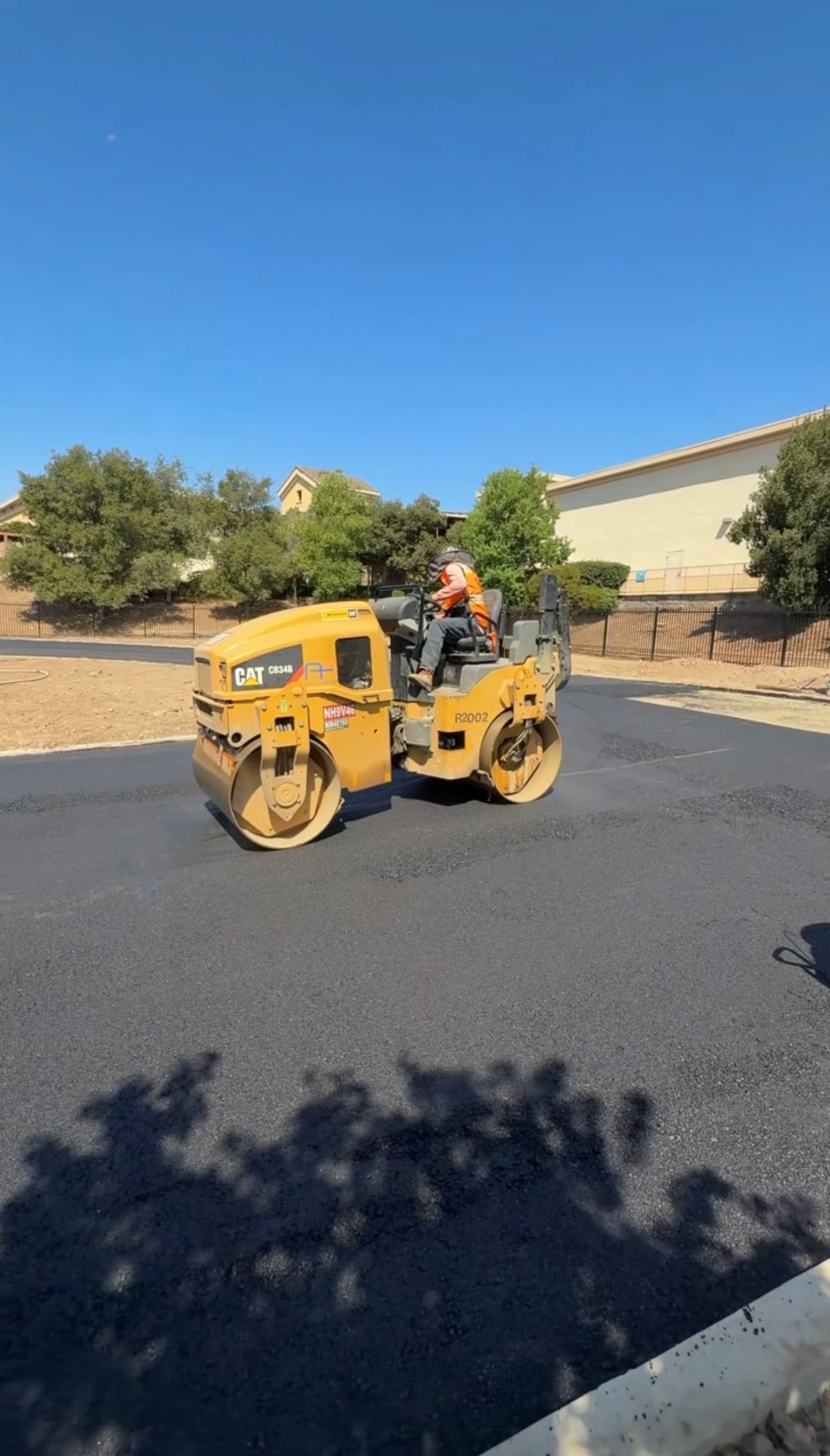 Yellow road roller compacting fresh black asphalt on a residential street in bright sunlight