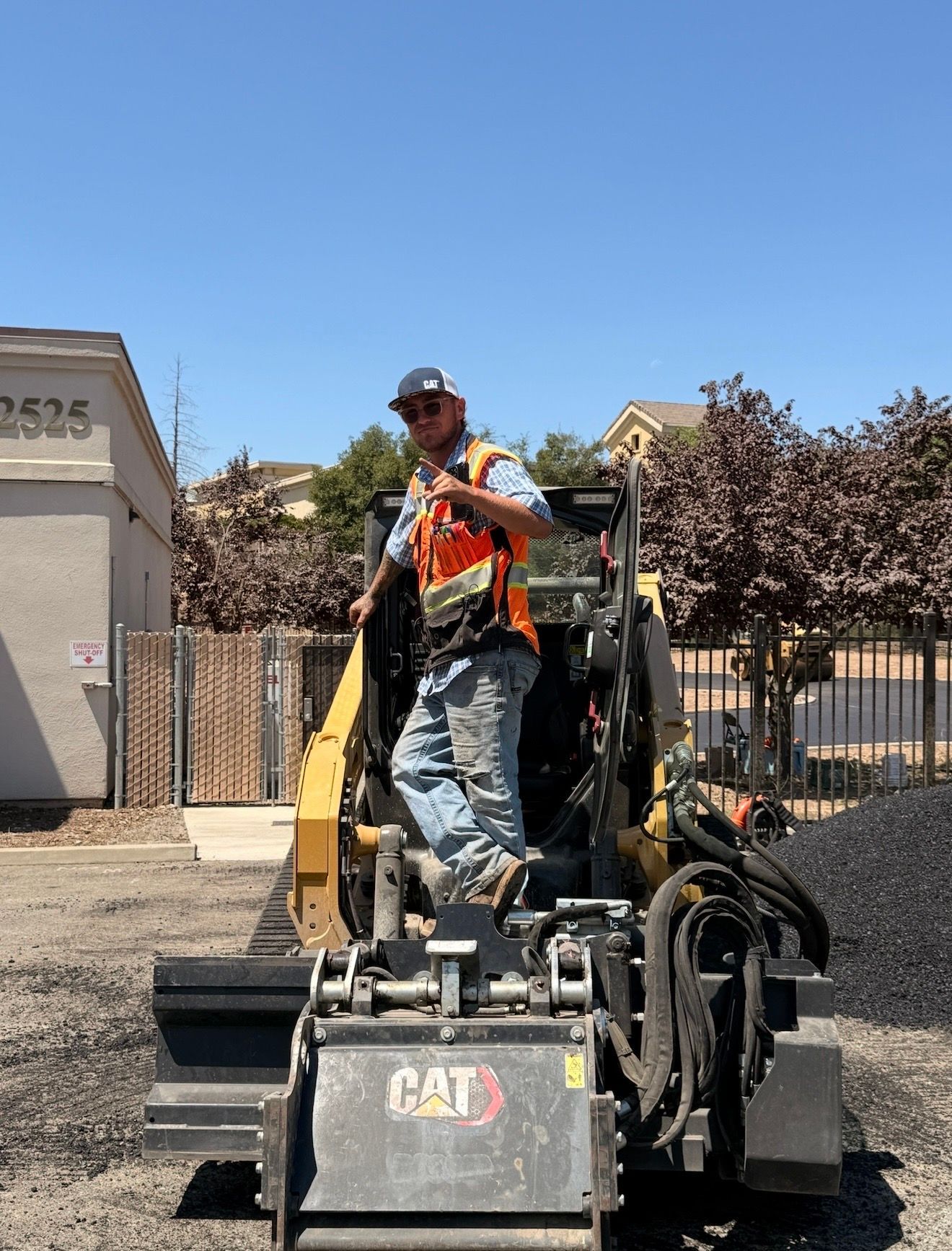 Worker in orange safety vest operating a CAT paving machine outdoors on a sunny day
