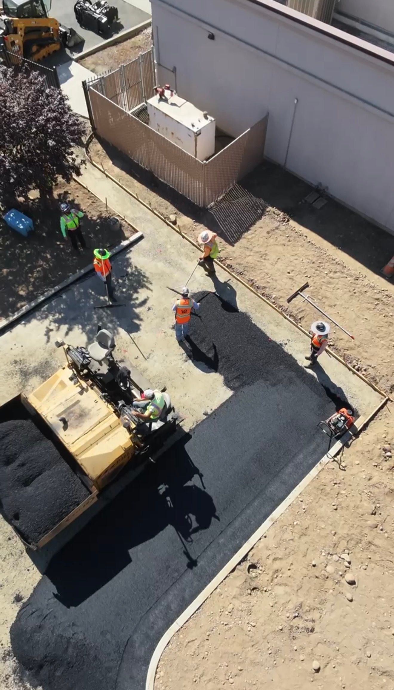 Overhead view of construction workers paving a curved path beside a building and dirt lot