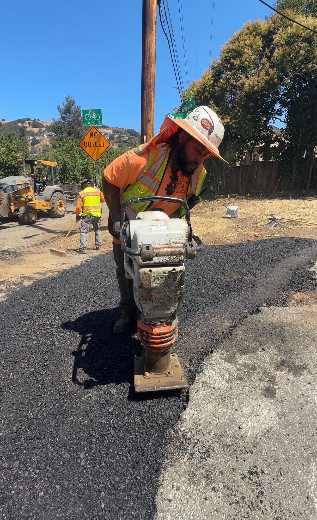 Construction worker operating a jackhammer on a road repair site under bright sun