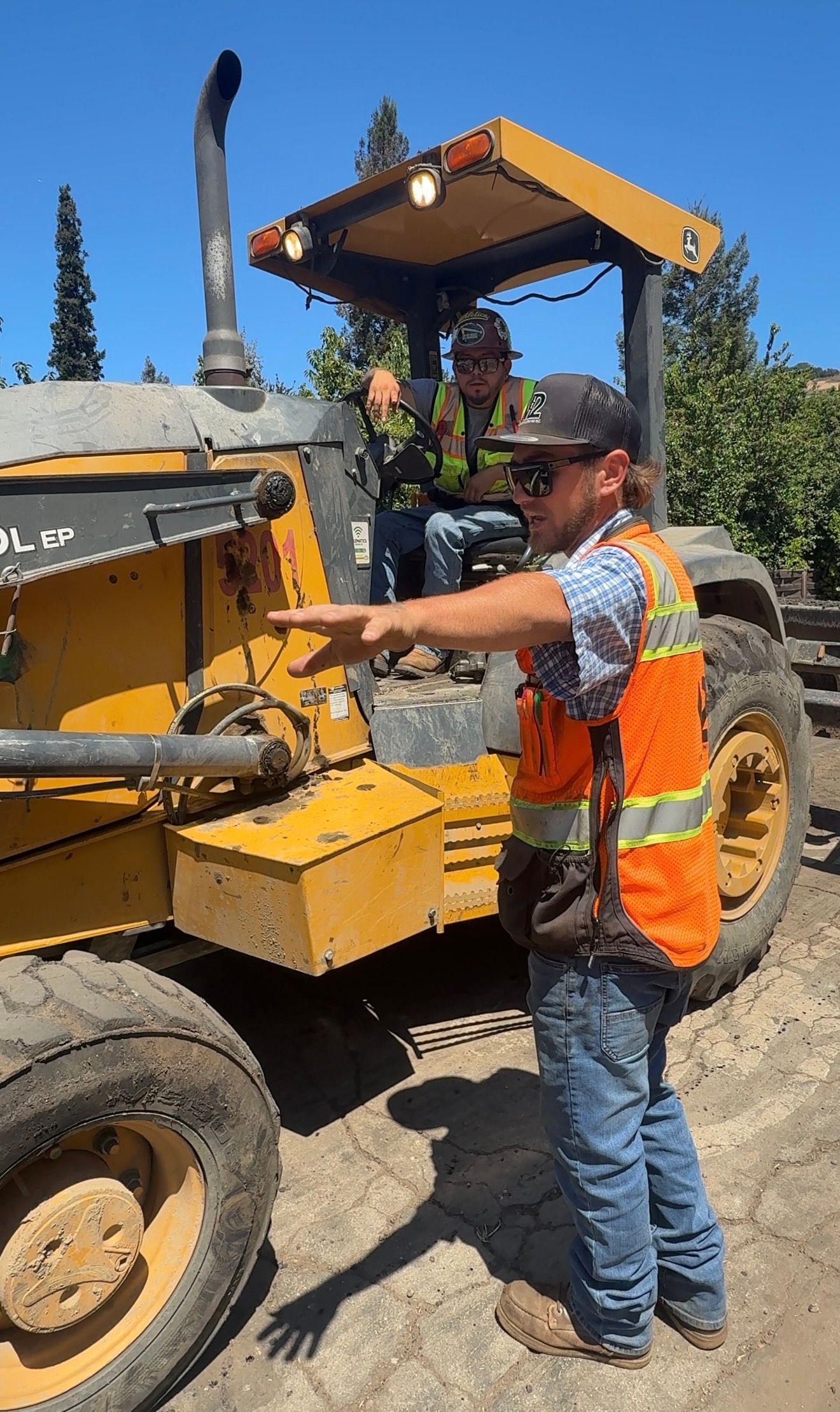 Construction worker operating a yellow road grader in a dusty outdoor worksite