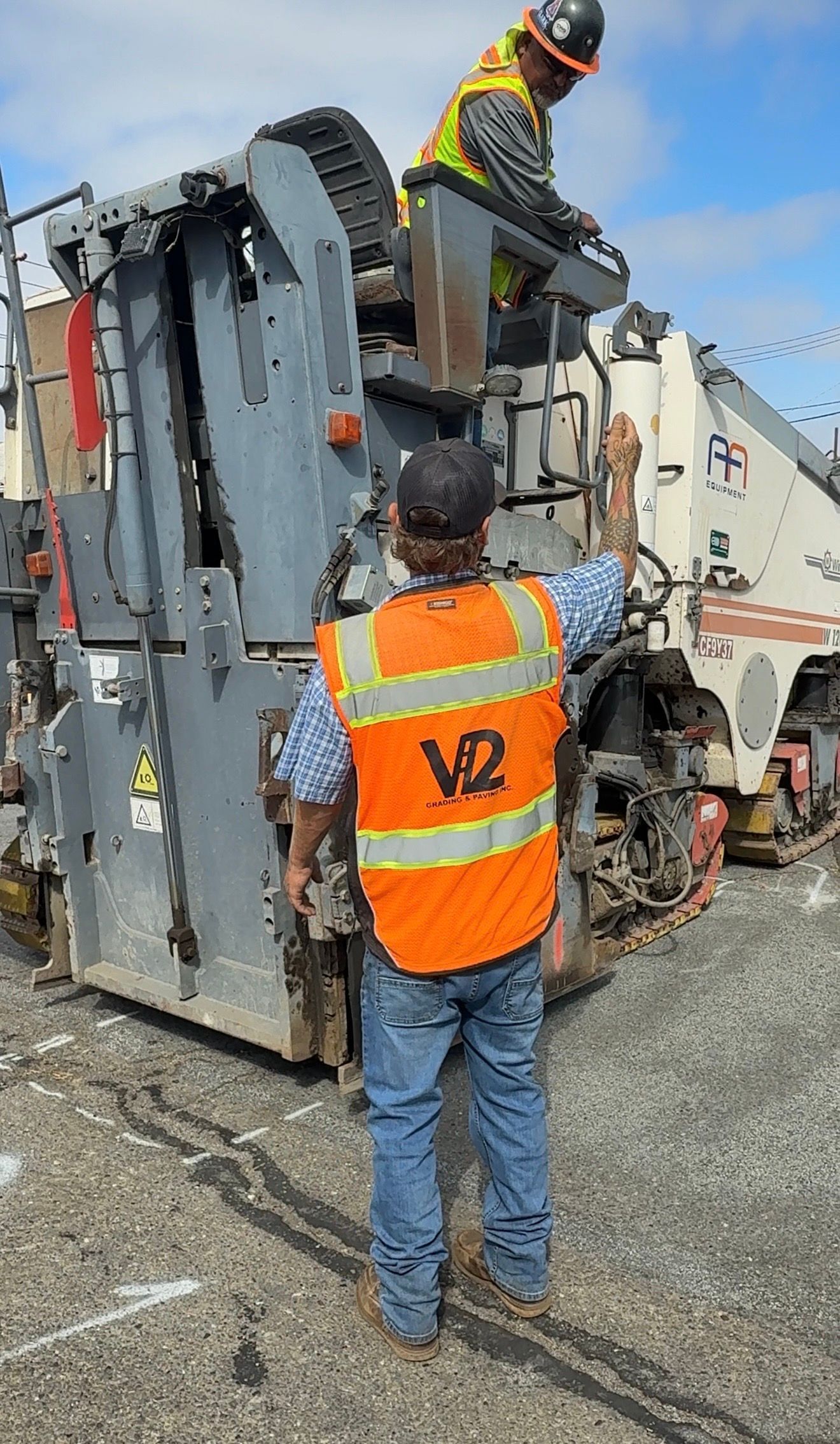Workers in orange safety vests inspect a tipped-over garbage truck on a roadside.