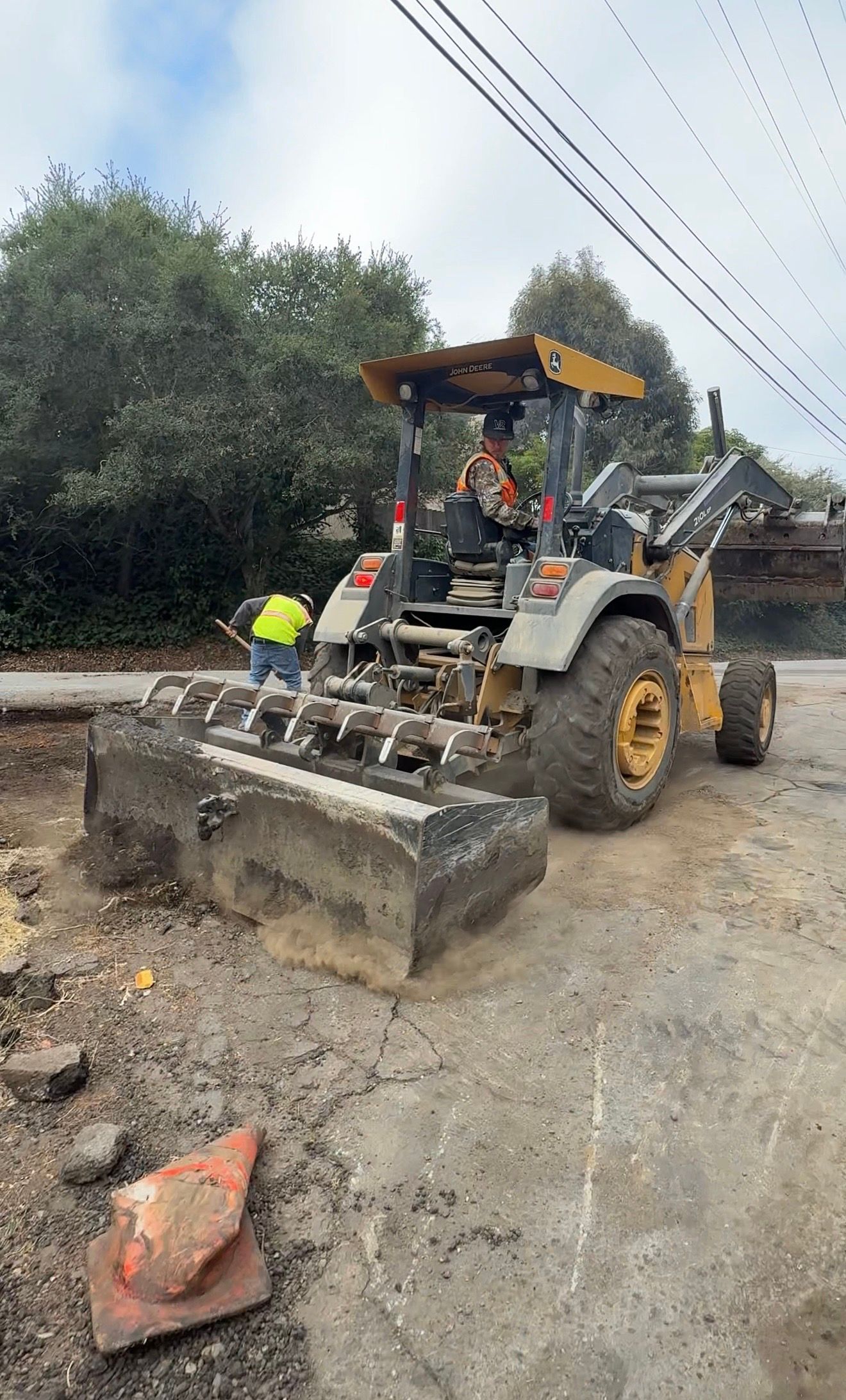 Yellow front loader bulldozer clearing muddy road debris beside power lines.
