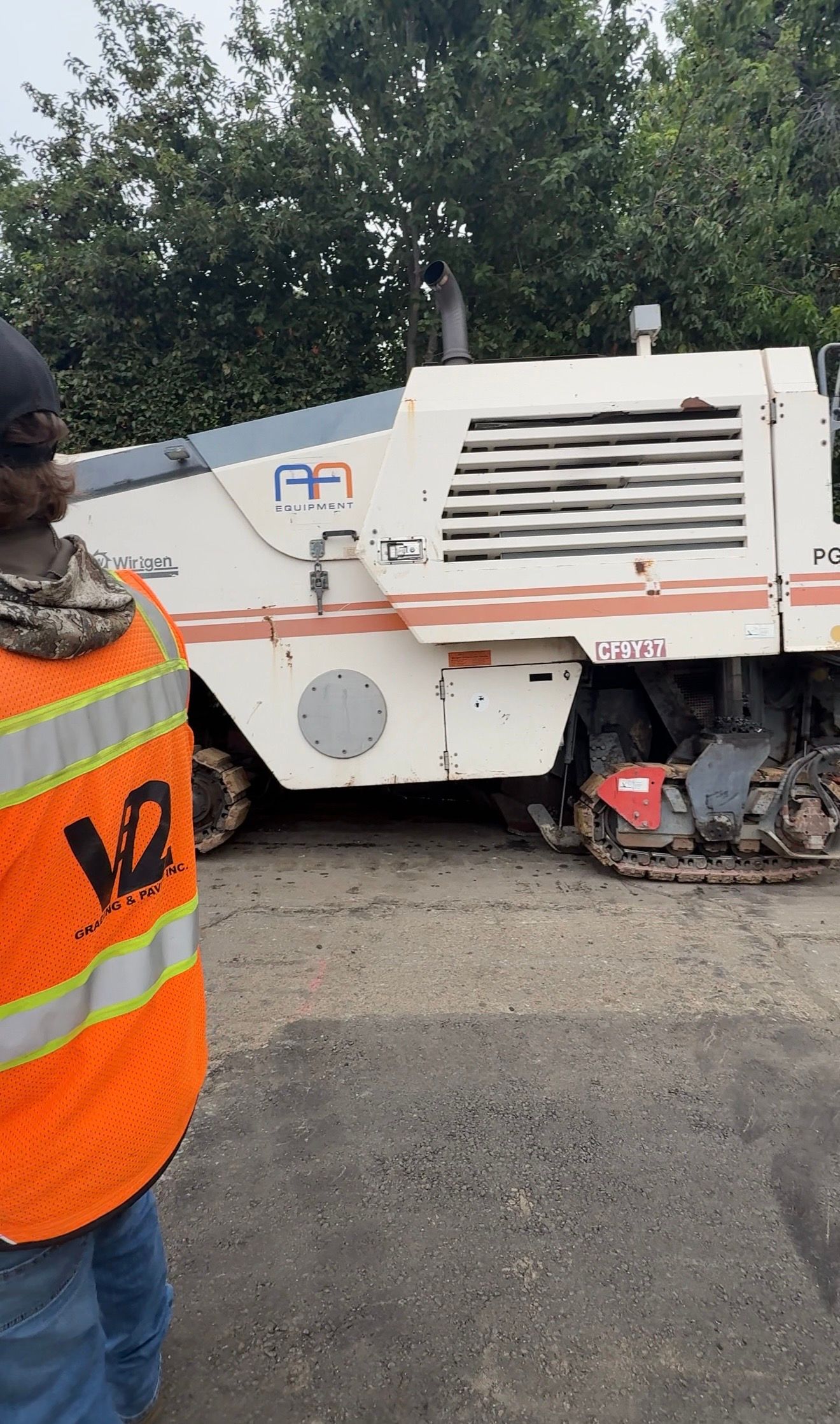 Street sweeper vehicle parked by roadside, partially obscured by a worker in an orange safety vest.