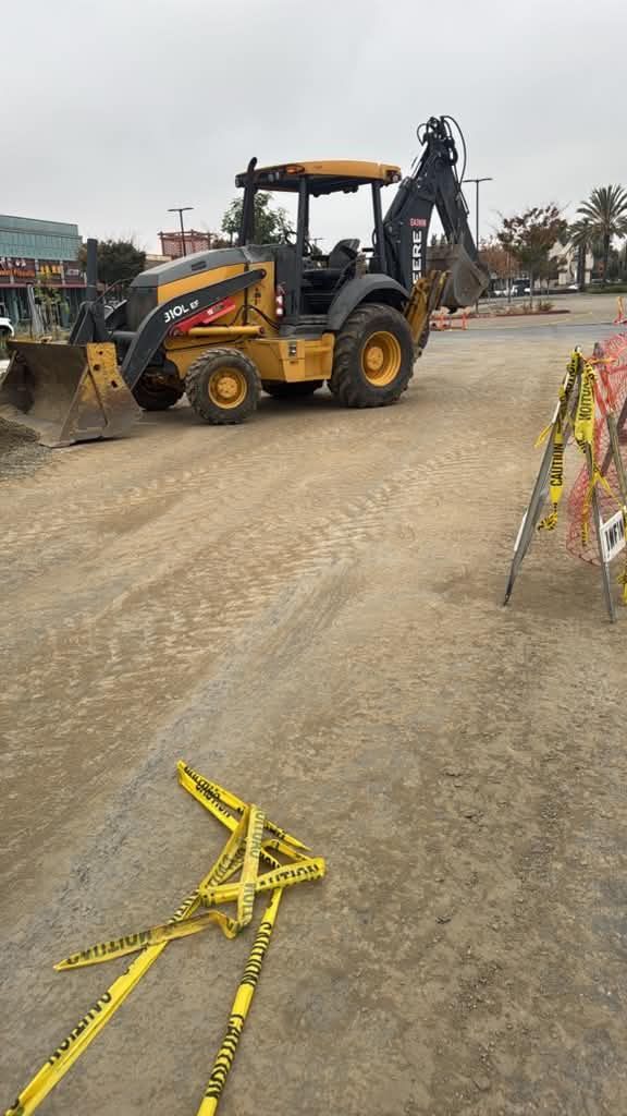 Backhoe loader on a dusty road near yellow barricade tape and an overturned barrier