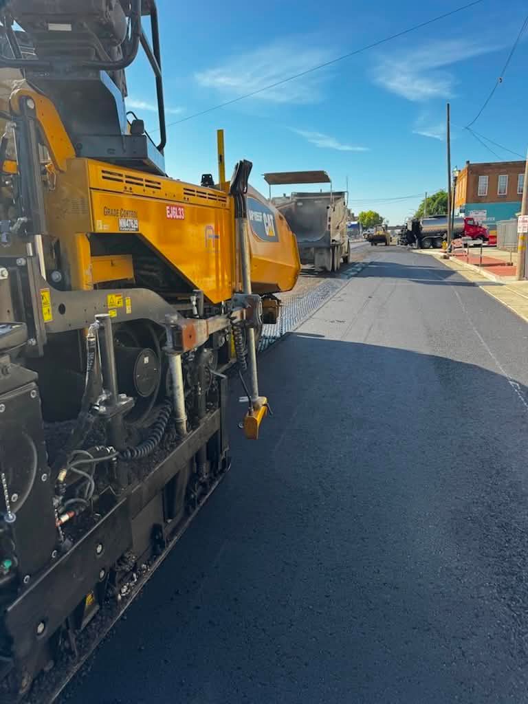 Yellow road paving machine on a street with workers and construction equipment nearby