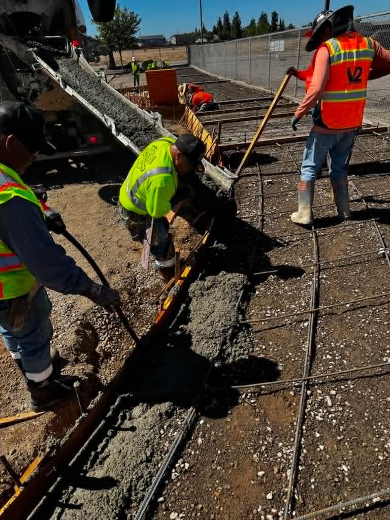 Workers in neon safety vests inspect a damaged utility trench beside broken pavement.