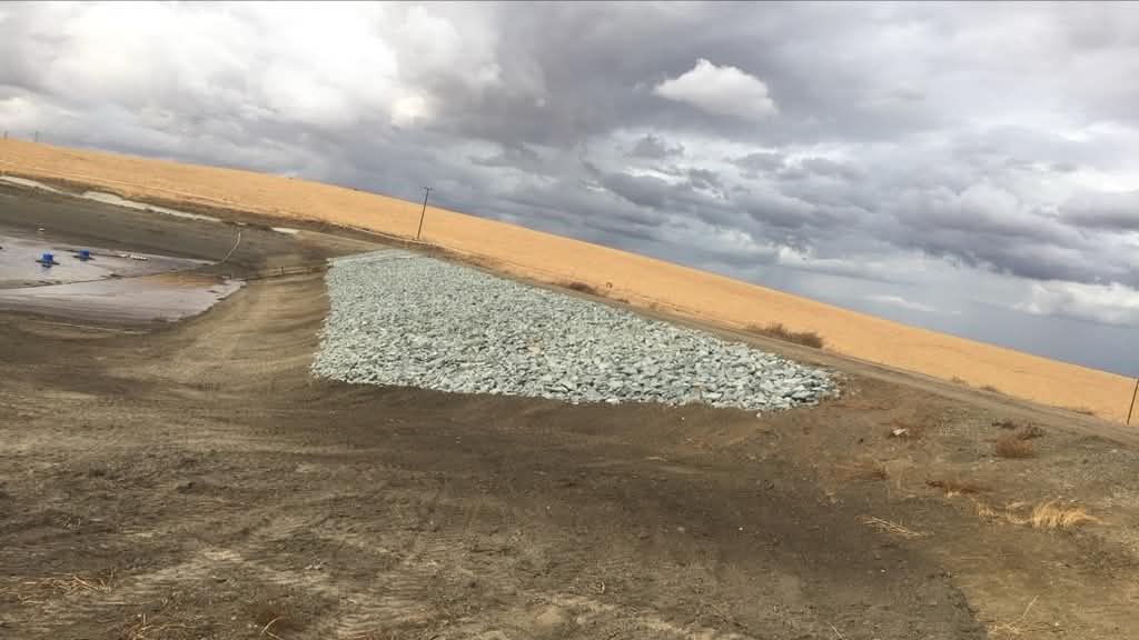Gravel mound on a desert road under cloudy sky, with sand dunes in the background