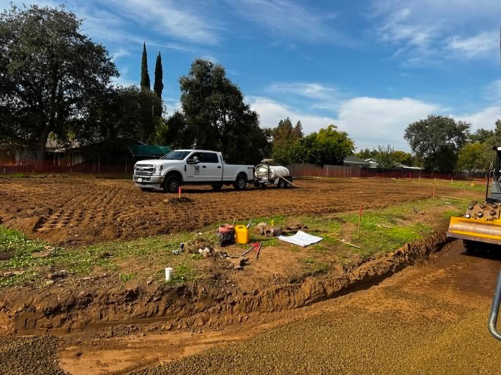 White pickup truck in a dirt field with construction equipment and trees under a blue sky