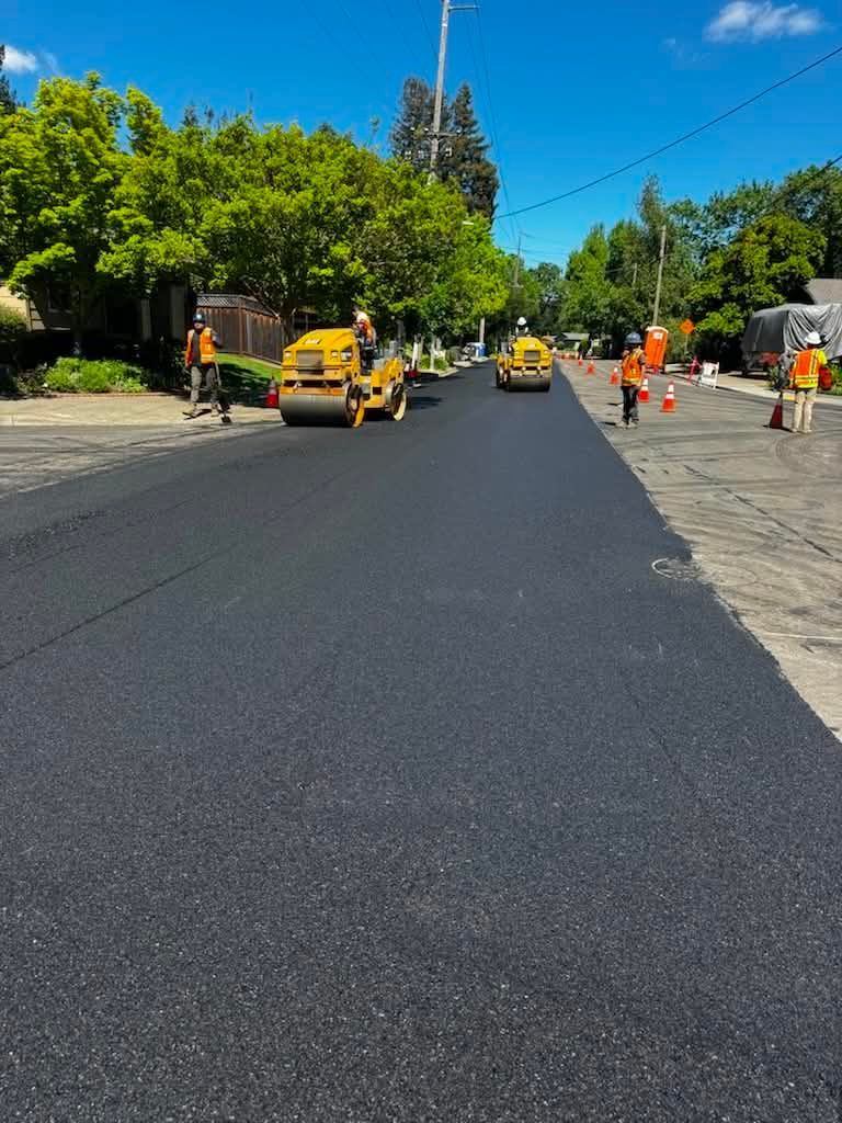 Freshly paved road with construction workers and equipment on a sunny day