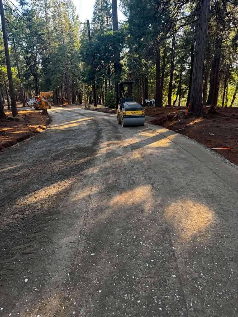 Curving gravel road in a wooded area with a small yellow car and construction equipment nearby