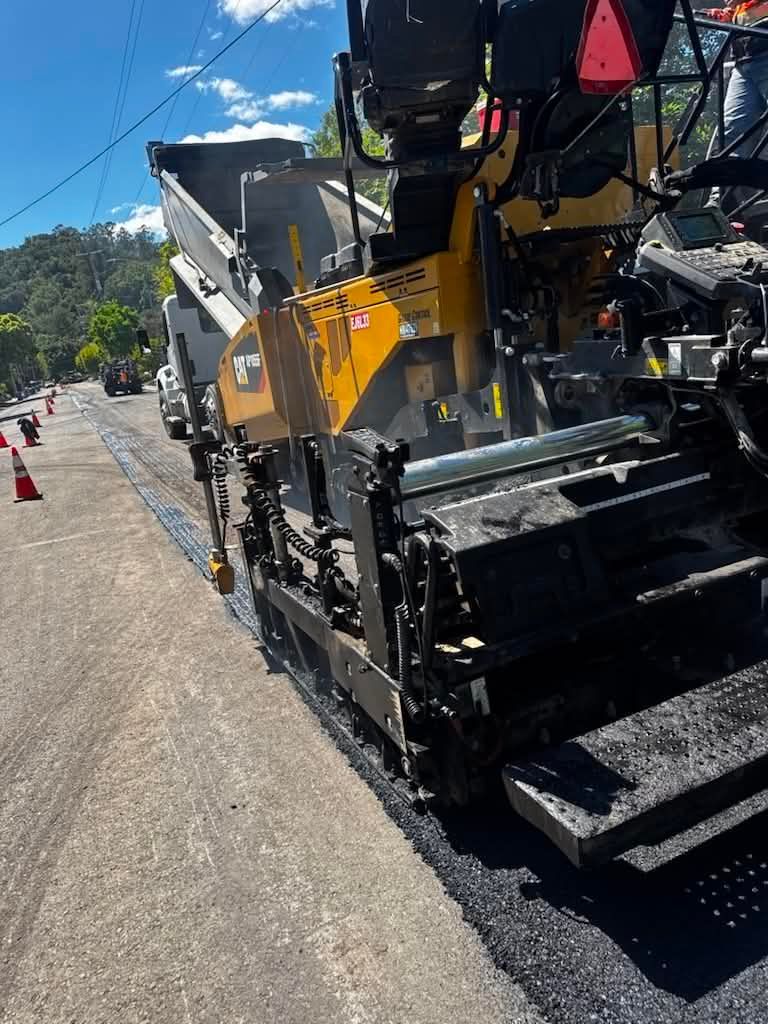 Road construction machine paving asphalt on a sunny street with workers nearby