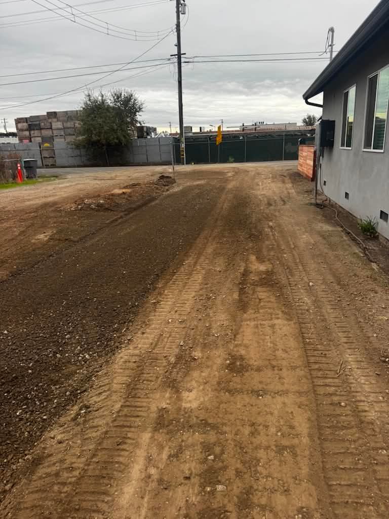 Dirt road leading to a gated entrance beside a gray building under overcast skies.