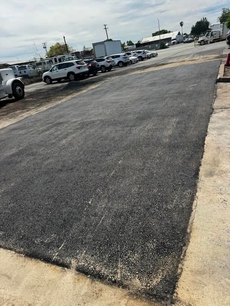 Empty paved parking lot with cars parked along the edge under a cloudy sky.