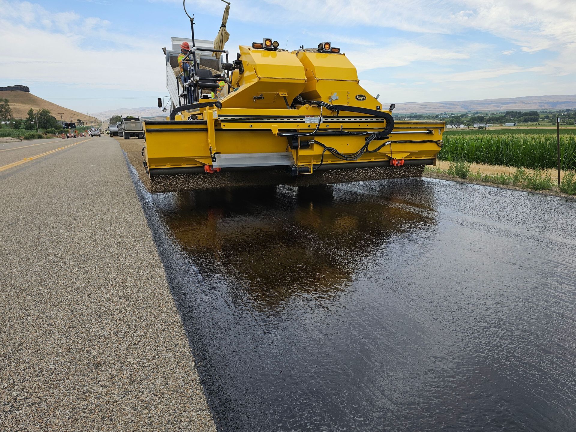 Yellow road paver spreading fresh asphalt on a rural road beside farmland