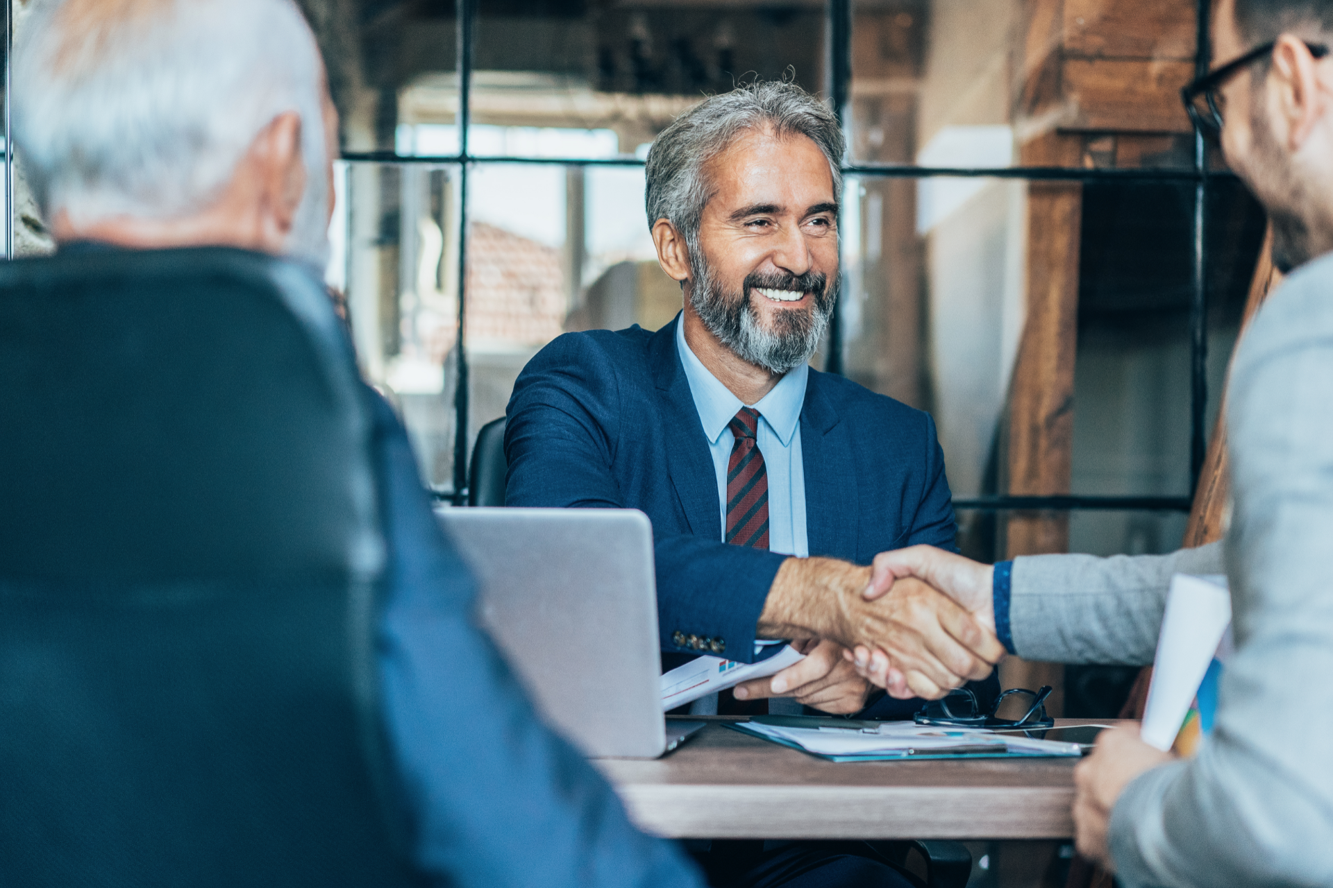 Business meeting in an office, with two people shaking hands across a laptop.
