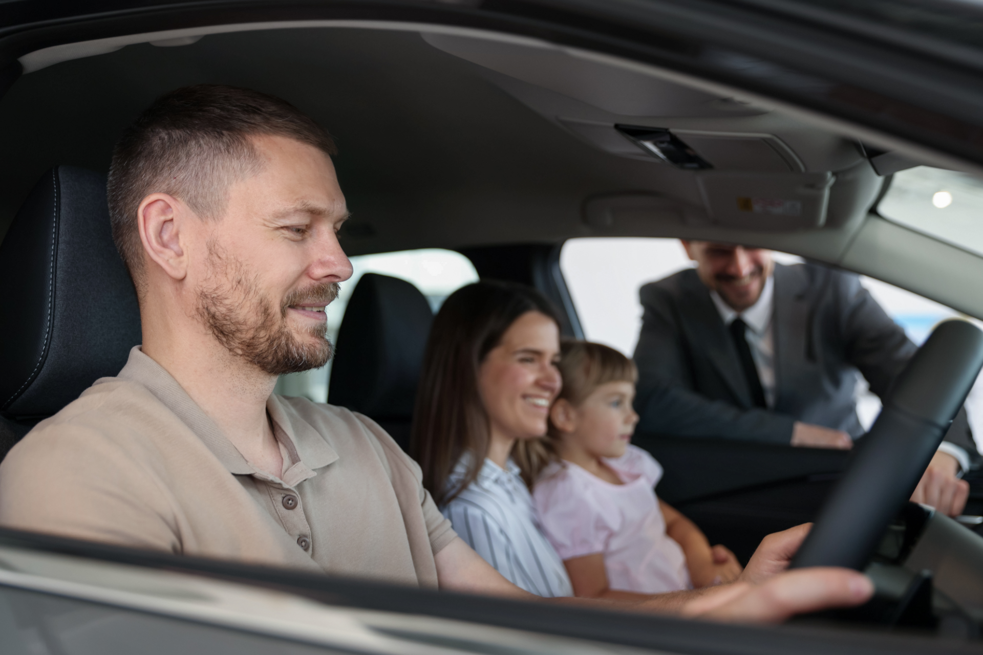 Man driving car, smiling, with family in the back seat.