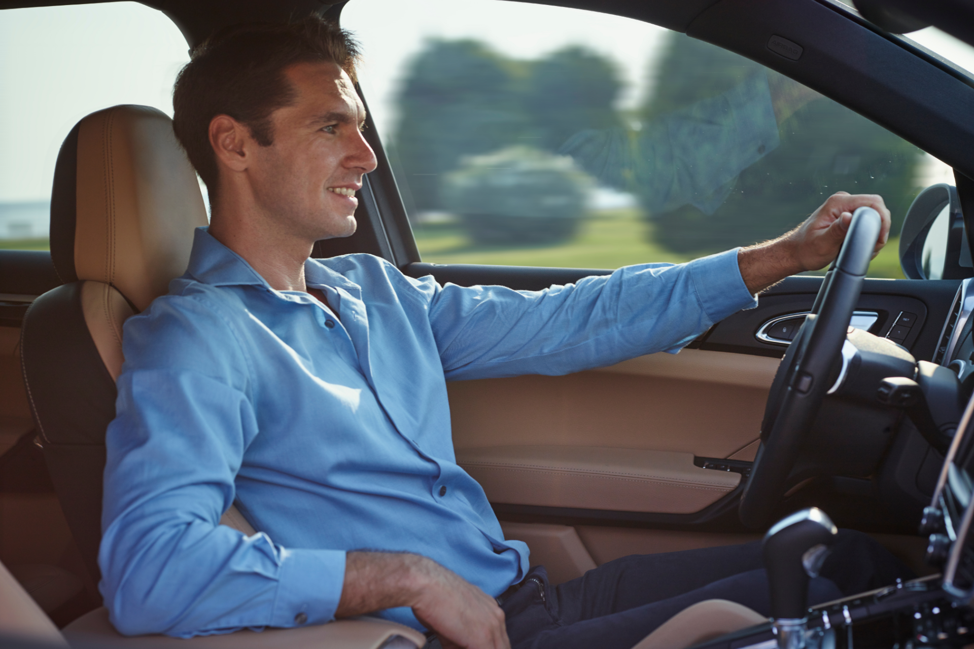 Driver in a blue shirt driving a car, seen from the passenger side.