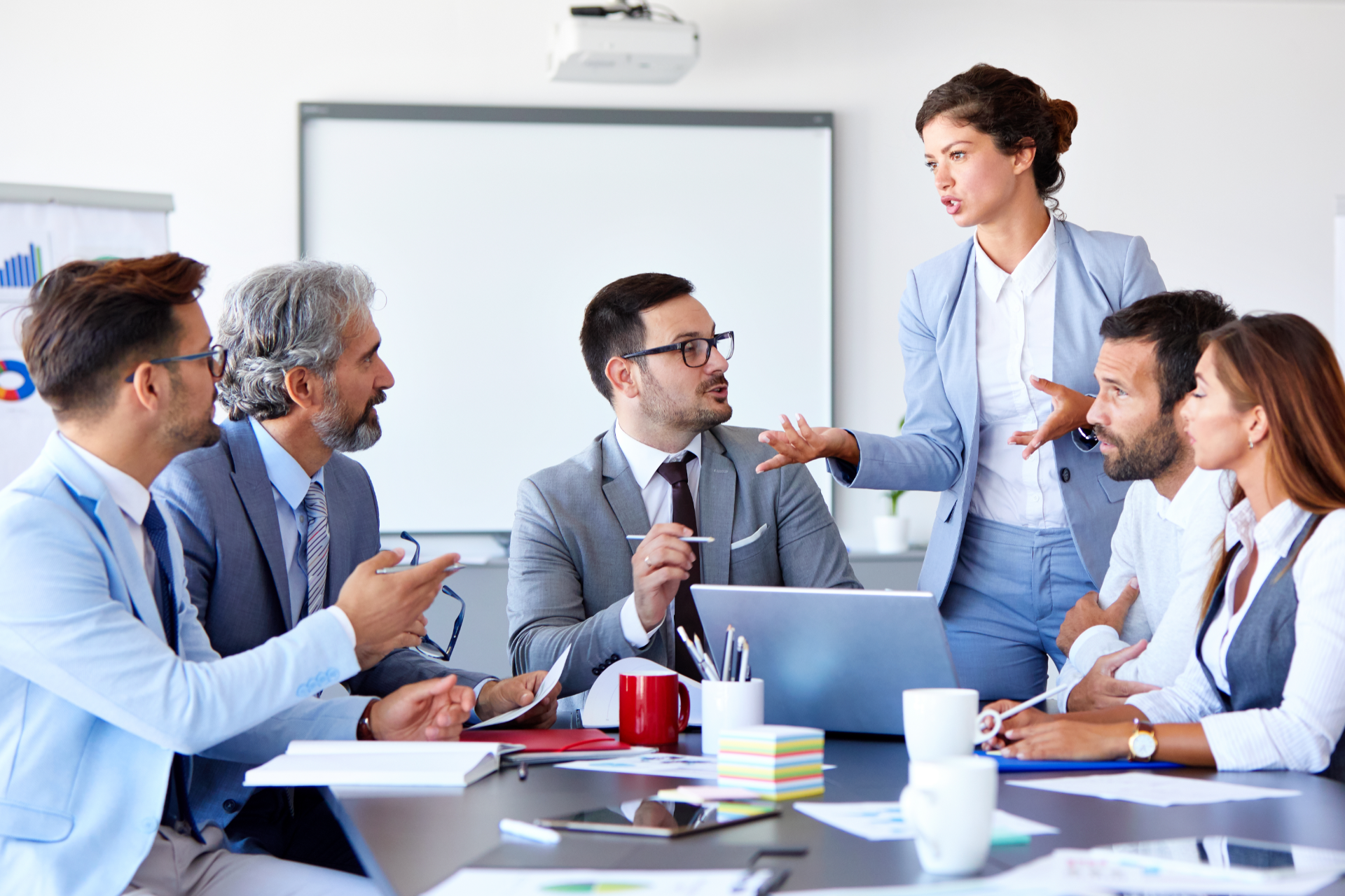 Business meeting in a bright conference room with six colleagues discussing around a table and whiteboard