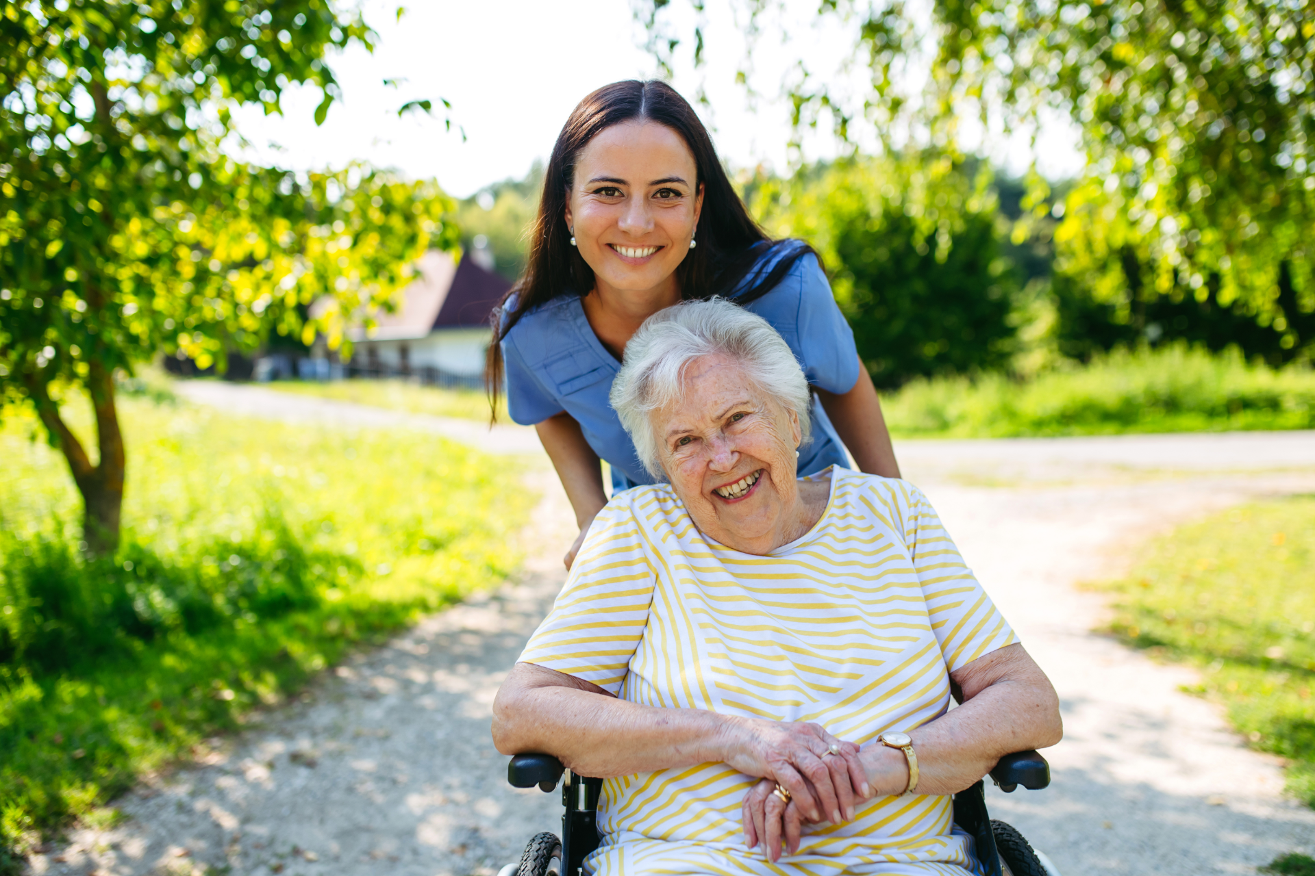 Woman pushing an elderly woman in a wheelchair along a sunny park path