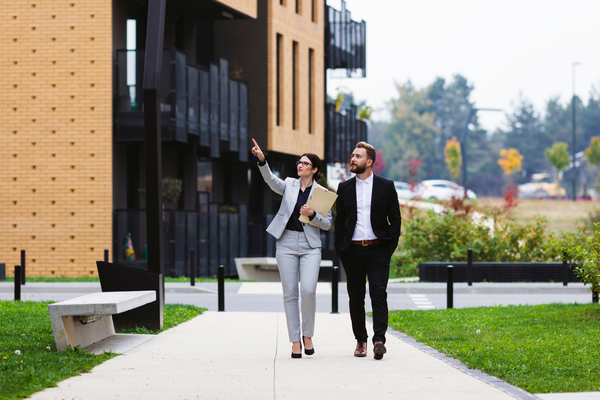 Two people in business attire walking and talking beside a modern office building outdoors.