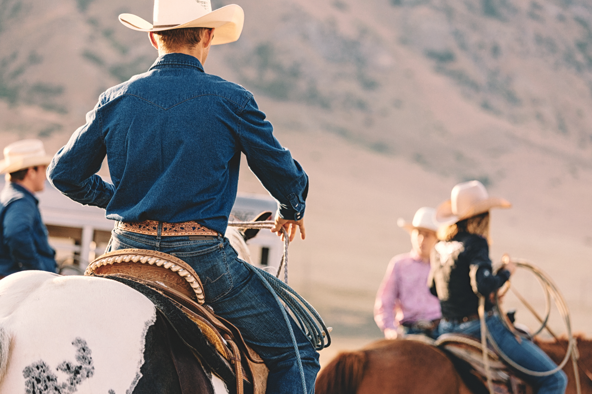 Cowboys on horseback in a dusty desert scene, viewed from behind.