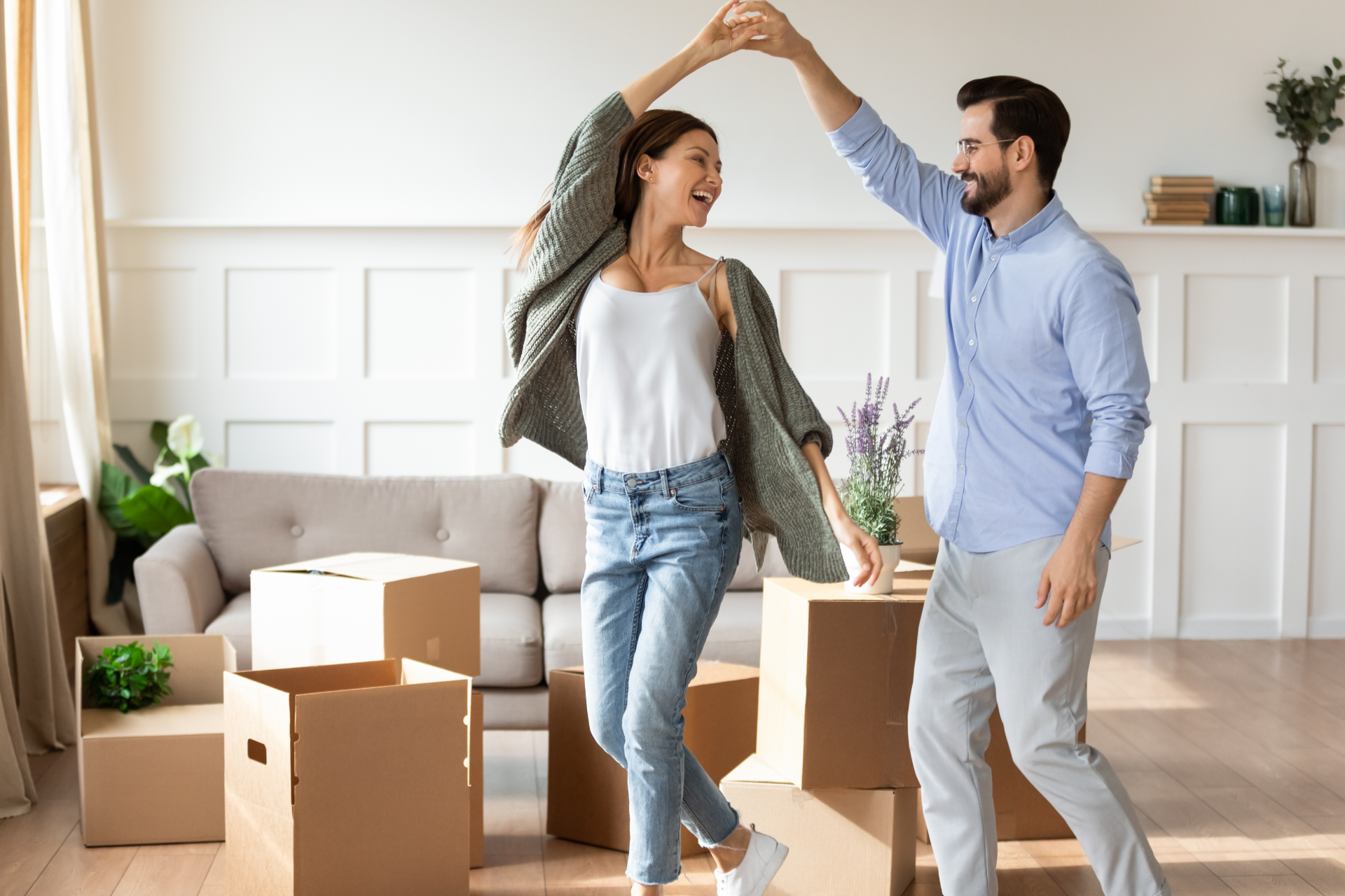 Couple dancing in a bright living room surrounded by moving boxes during a home move