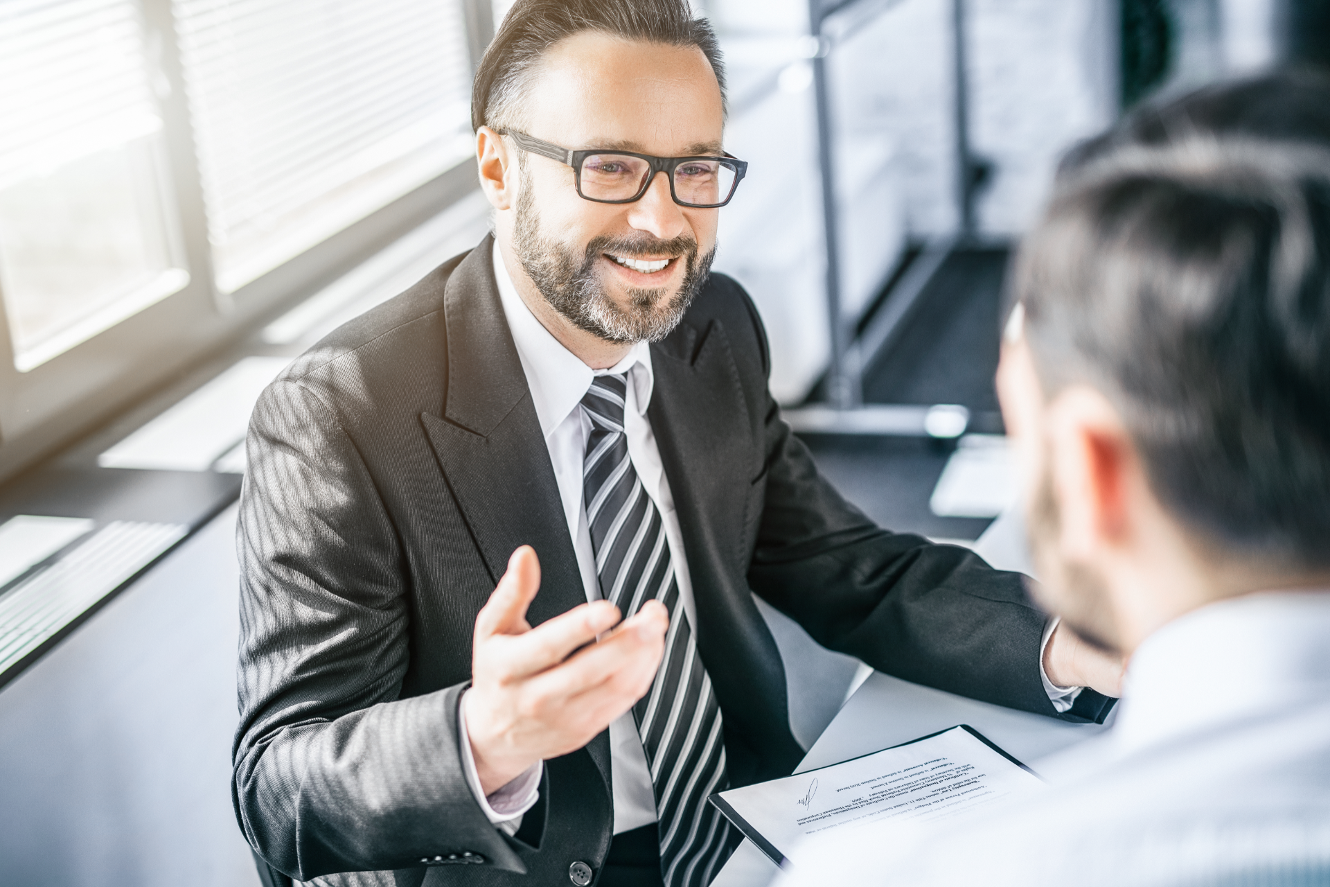 Two businesspeople in a bright office, one smiling and gesturing during a meeting