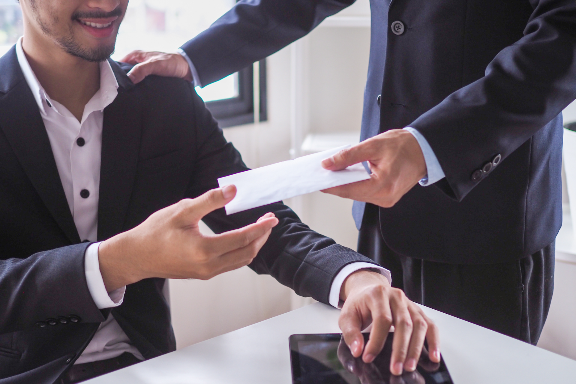 Two businesspeople exchanging a document at a desk in a bright office